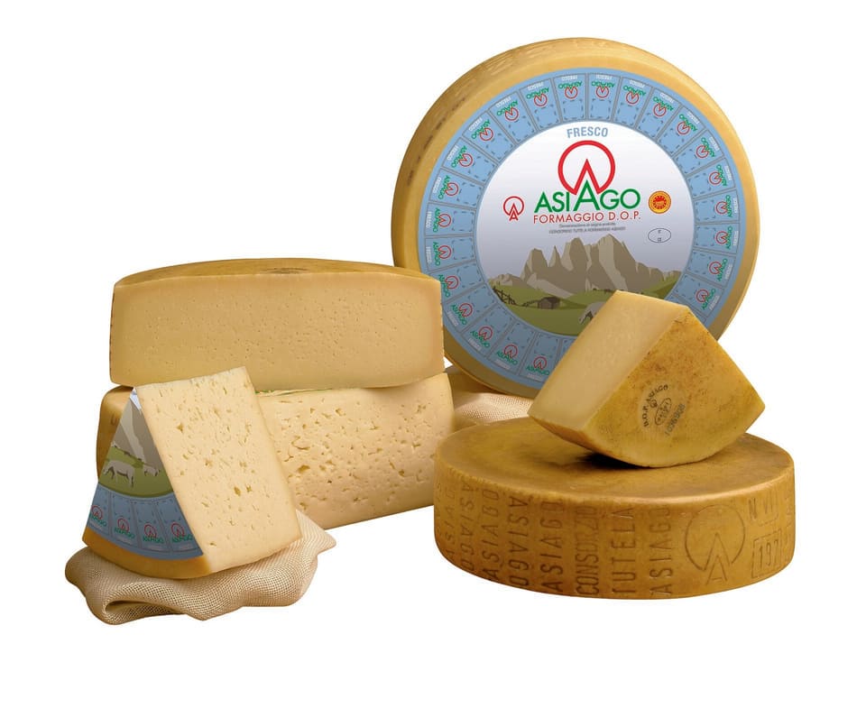 Головки и куски Азиаго: светлый молодой Asiago Fresco с неровными глазками и выдержанный Asiago Stagionato с надписью ASIAGO на боку