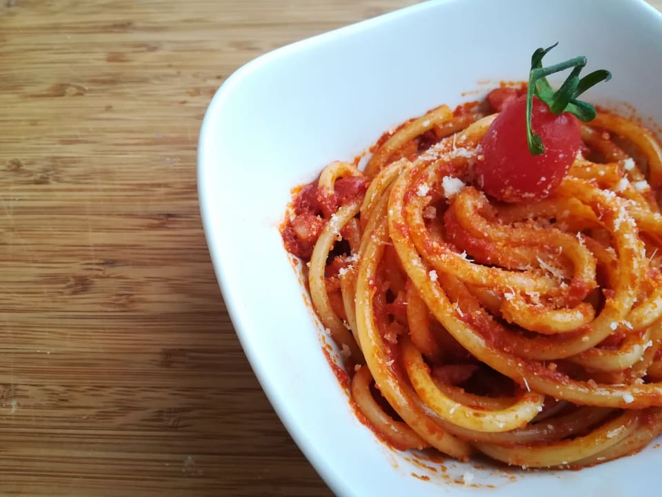 Букатини аматричана с томатным соусом и сыром в белой тарелке