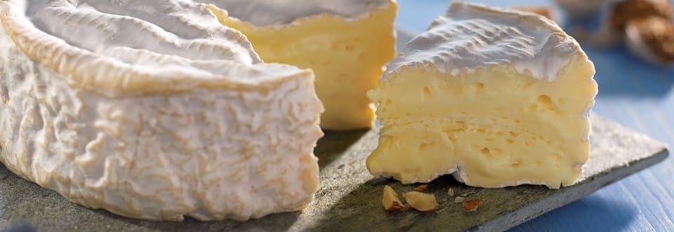 Головка камамбера с белой коркой и отрезанным куском, мягкое кремовое тесто