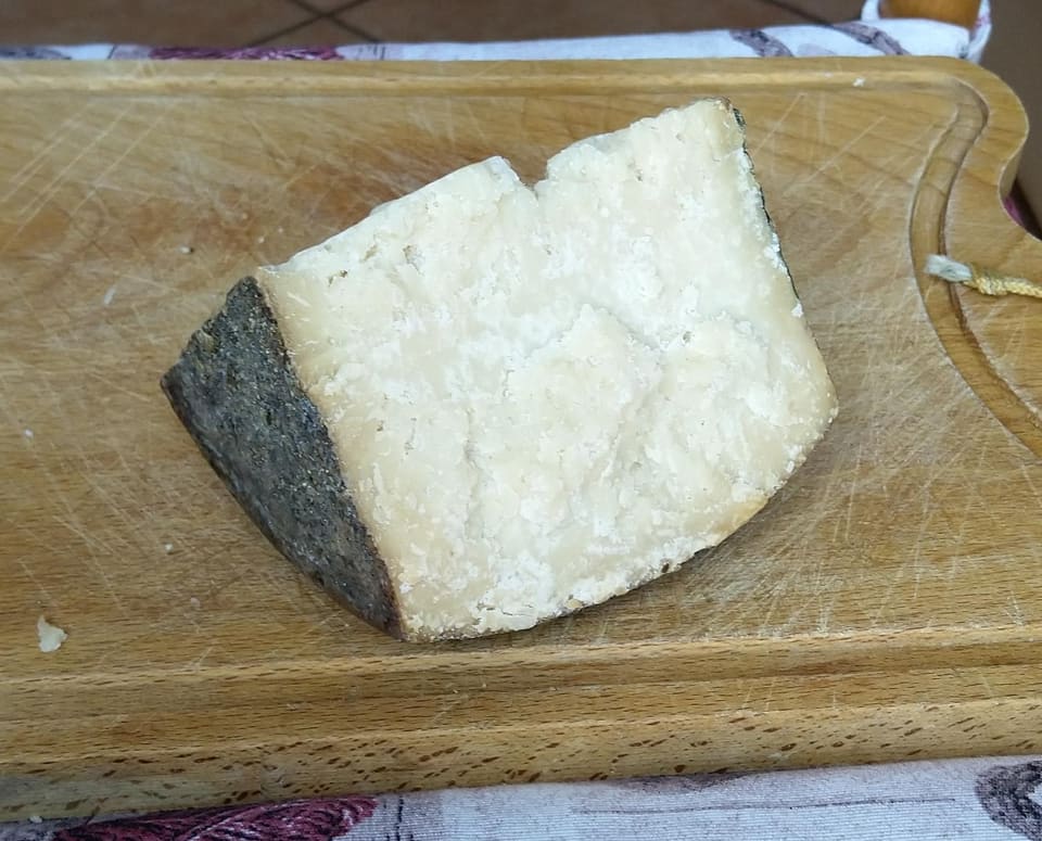 Кусок сыра Фьоре Сардо с тёмной коркой и белым плотным тестом на деревянной доске