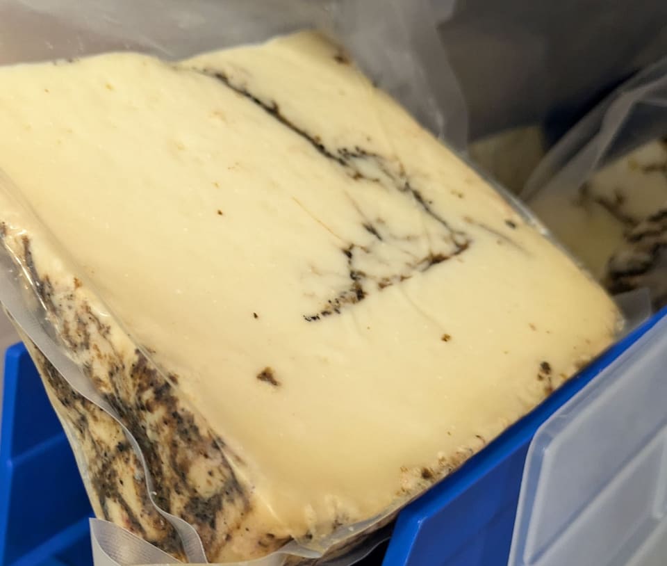 Кусок овечьего сыра с чёрными прожилками трюфельной пасты в вакуумной упаковке
