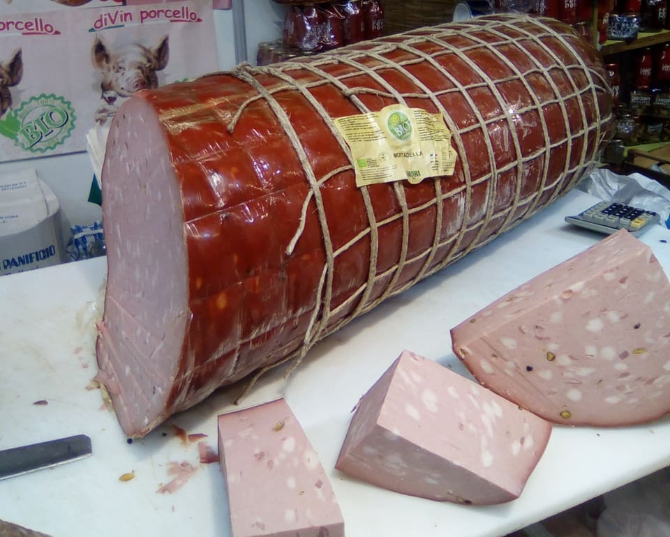 Большая мортаделла в разрезе: розовое мясо с белыми кубиками шпика