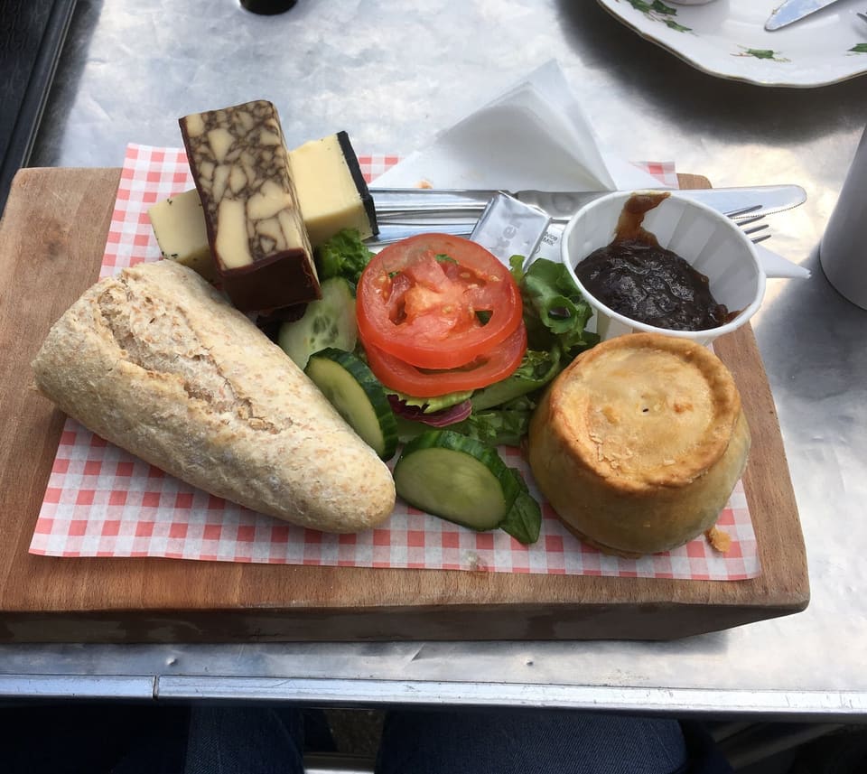 Доска с хлебом, двумя кусками сыра, помидором, салатом, соусом и пирогом со свининой